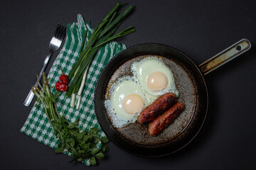 Scrambled eggs on a dark background. Fried eggs with fried sausages. Tasty breakfast. Unhealthy...