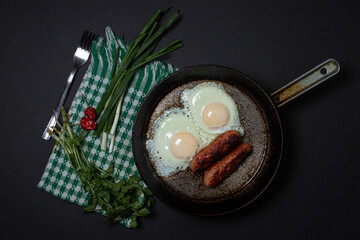 Scrambled eggs on a dark background. Fried eggs with fried sausages. Tasty breakfast. Unhealthy...