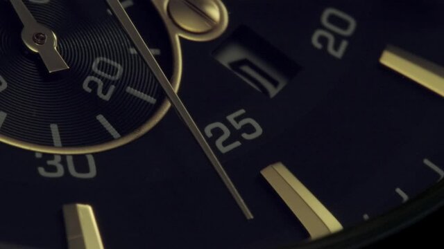 Light is flickering on swiss watch with second counter and chronograph. Golden arrow is running by numbers on clockface. Extreme closeup view