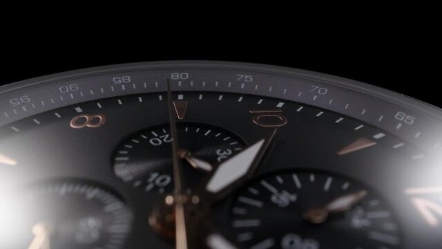 Black clockface with chronograph and stopwatch rotating while camera is following the golden second arrow. Swiss watch with tachymeter closeup, macro view on black background 