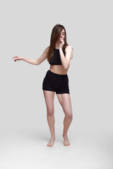 Fototapeta premium Young slim athletic girl, with long hair, in a black top and shorts, in the studio on a white background