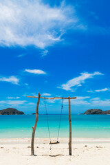 Obraz na płótnie Canvas swing made of logs on an idyllic beach of clear sand with crystal clear water on a sunny day with a blue sky. vertical image. summer concept. travel concept.