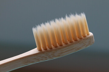 A closeup photo of a bamboo toothbrush on dark gray background with naturally colored bristles. Plastic free zero waste product. 