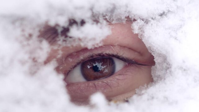 a close-up of the female eye peeps out from under the snow. snowflakes melt on the skin of the eyelid and spread over it. the image of a person after winter or before spring. Macro Shot Opening and