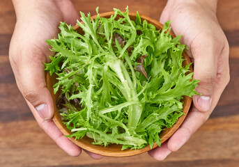 concept of a healthy man hand holding a wooden bowl of fresh leaves salanova salad on wood table background                        