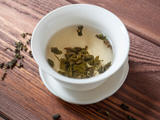 green tea is brewed in a white bowl on a wooden background. Dry tea leaves lie nearby. Top view