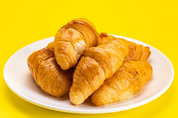 Pile of freshly baked croissants in white ceramic dish on yellow background with clipping path.