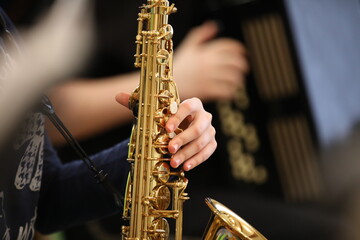 A young hand of a student musician saxophonist with his fingers presses the valves of a golden...