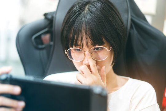 Young adult asian gamer woman wear eyeglasses play a handheld online game.