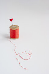 Sewing needle with red heart at the end and vintage wooden spool of thread