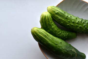 Three green cucumbers on a plate on a white background