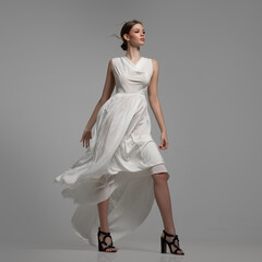 Fashion woman posing in white dress in full growth. Gray background