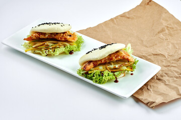 Appetizing Asian dish - steamed bao buns with chicken, vegetables on a white plate on a white plate. Street food. Bao burger