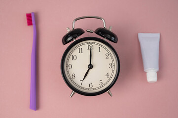 Fototapeta na wymiar Toothbrush, tube of toothpaste and alarm clock on a pink background. Time to brush your teeth.