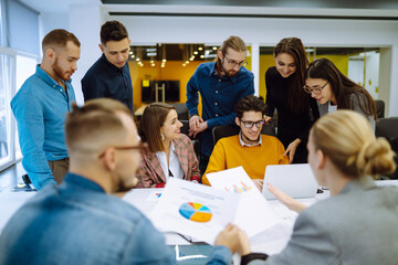 Group of young modern people working on project together. Business colleagues discuss financial result review paperwork share ideas brainstorm collaborate work in teamwork. Planning, analysis.