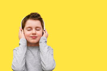 Smiling boy listens to music with headphones. A cute boy in a gray t-shirt holds a white wireless...