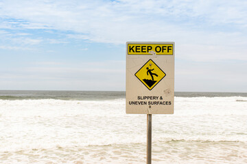 Warning sign Keep Off - Slippery and Uneven Surfaces near the ocean