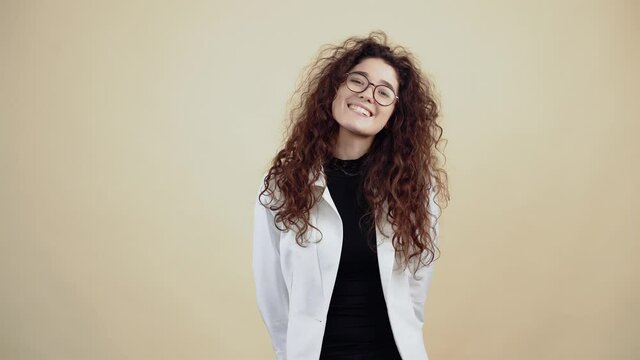 Shy young woman with curly hair smiles with her teeth and looks into the room. Young hipster in gray jacket and white shirt,