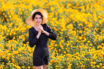 Naklejka na ściany i meble Beautiful Asian woman wear black dress ane hat walking in marigold flowers garden.