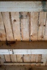 Grunge rough wooden ceiling in a perspective view with colorful stains of fungus and moist and jars in wood. Beamed ceiling in a shed or attic or old wooden cabin.