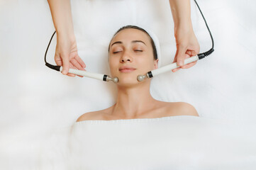 Top view of middle aged woman receiving electrical stimulation facial skin care spa procedure....