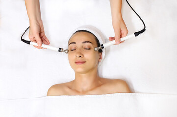 Top view of middle aged woman receiving electrical stimulation facial skin care spa procedure....