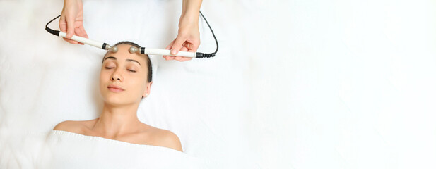 Top view of middle aged woman receiving electrical stimulation facial skin care spa procedure. Microcurrent lift face.