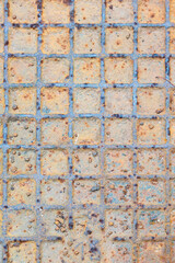 Texture of colorful old rusty lid of a canalization drain with a chequered pattern. Part of metallic doors closing the sewage.
