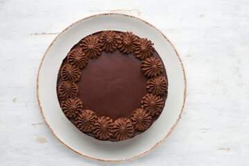 top view of round baked chocolate cake on a light wooden background.