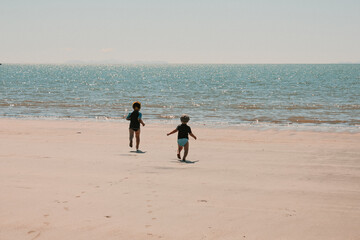 Two little boys running towards the water on the beach during a tropical holiday at Queensland,...