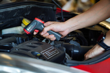 technician's hand holds a digital thermometer, which measures the heat of the engine.Motor temperature measurement in the car service