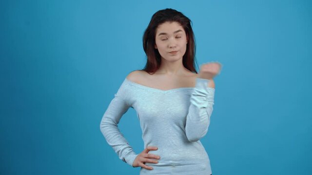The unwell Asian girl says no, with her hand in front of her, moving her index finger. With dark hair, dressed in a blue blouse, isolated on a dark blue background in the studio