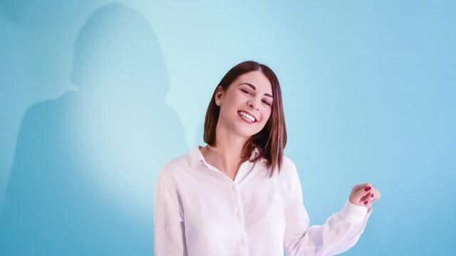 Beautiful caucasian woman with brown hair wearing white shirt dances against blue background. White teeth smile. 4K Resolution video.