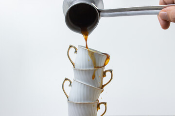 Coffee is poured into a stack of coffee cups. Boiled coffee on a white background. Coffee cups on top of each other