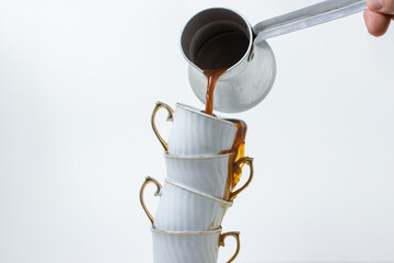 Coffee is poured into a stack of coffee cups. Boiled coffee on a white background. Coffee cups on top of each other