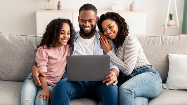 Happy African American family using laptop sitting on the couch