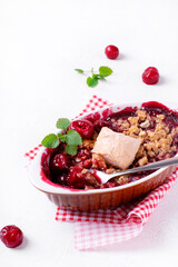 Crumble dessert with cherry served with ice cream in ceramic baking dish. British cuisine dessert