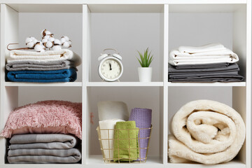 Organization of storage. Stacks of towels, sheets, bed linen, blankets and pillows on a white shelf.