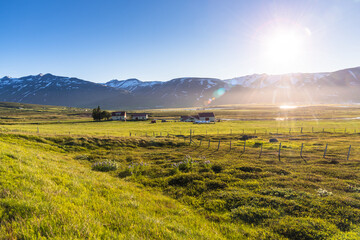 Farm in a grassy field in a rural landscape with snow-capped mountains in background in Iceland on...