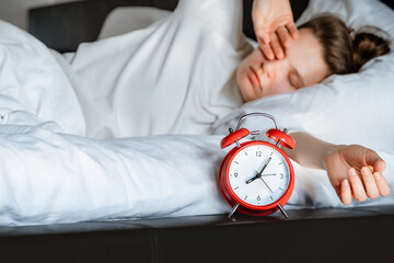 sleepy young millennial woman waking up in white bed yawning rubbing eyes turning off red vintage...