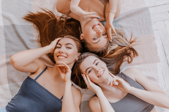 Women rest and have fun. Girlfriends laugh at home lying on the floor on pillows. Tree girls make homemade face and hair beauty masks. Women take care of youthful skin.