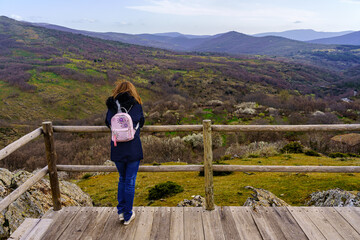 Fototapeta na wymiar Woman with her back turned at a viewpoint contemplating the views of the green mountain landscape. La Hiruela Madrid.