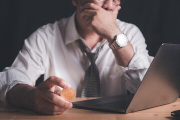 businessman hold Bitcoin and watches the laptop with stress due to losses from trading Bitcoin.