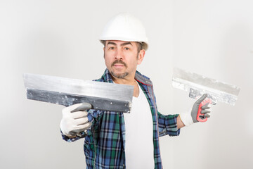 Builder in safety helmet with two putty knifes on white wall background