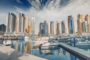 yacht and motor boats parking at the port near Dubai Marina Mall with row of high skyscrapers...