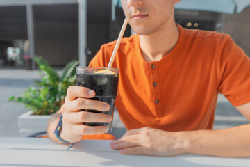 Man drinks unusual sparkling water in black color with ice and lemon with a drinking straw