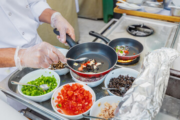Chef gloved hands cook vegetables and other ingredients on a gas stove in a frying pan