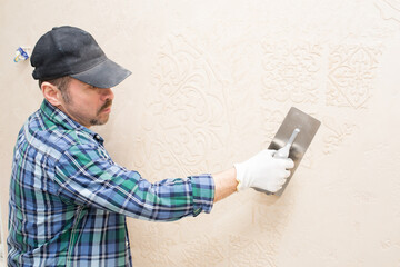 Builder repairman plasterer, applies decorative plaster, pattern on the wall, during renovation,...