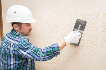 Builder repairman plasterer, in a protective helmet, during the repair applies decorative plaster,...