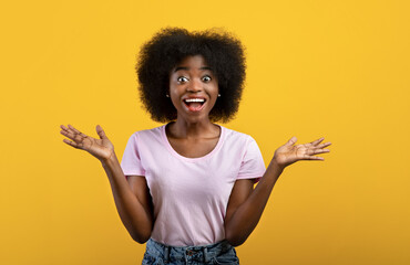 Omg. Overjoyed african american lady shouting in excitement and looking at camera, posing over yellow studio background